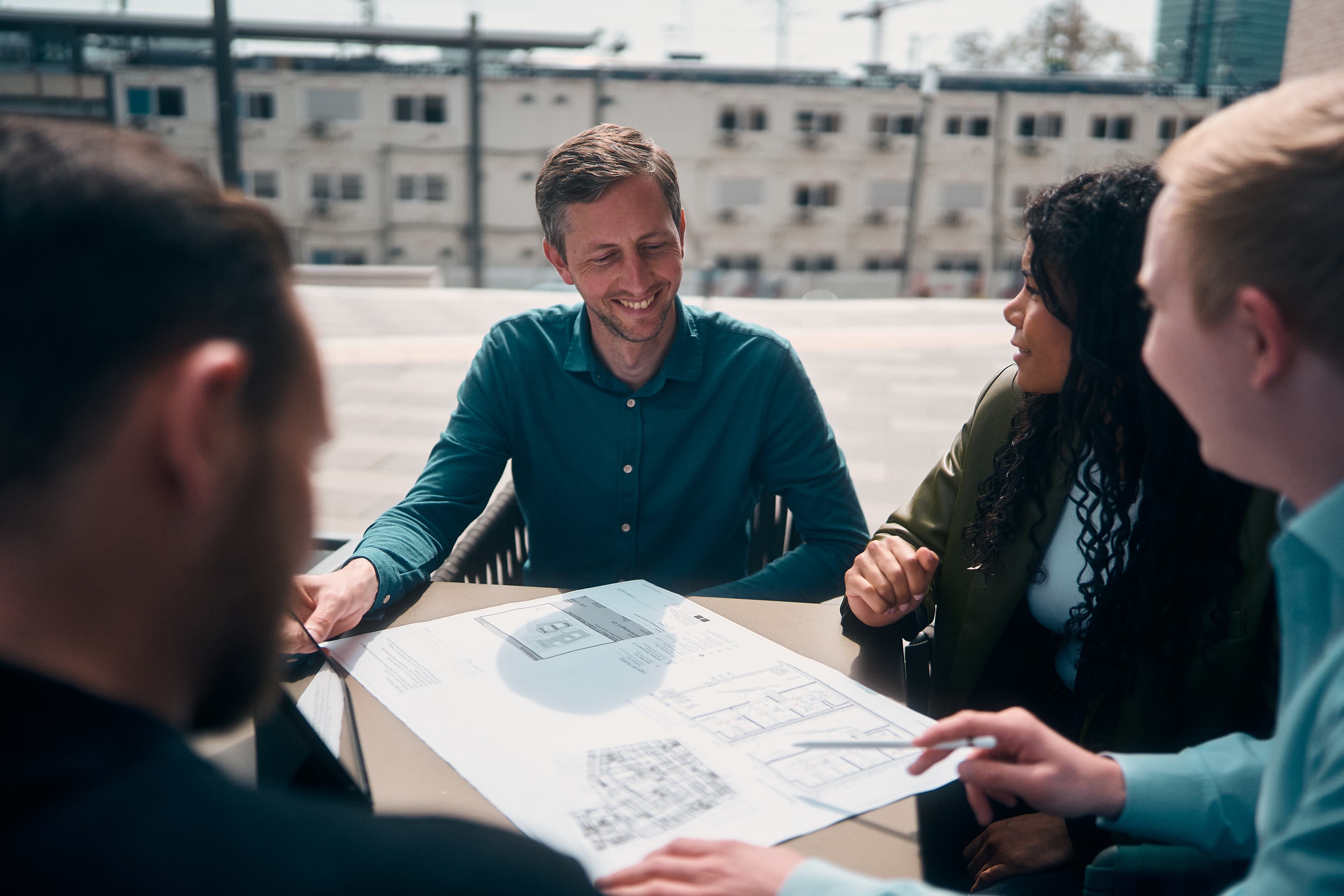 Vier Personen am Tisch betrachten einen Bauplan im Detail
